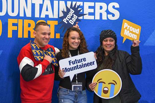 New student and family pose with WVU props in the Mountaineers Go First photo booth