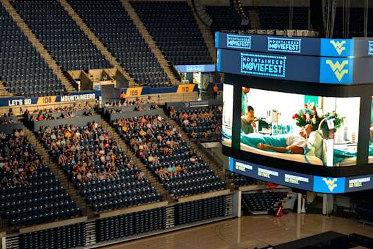 Students sit inside the Coliseum watching a movie on the main scoreboard.