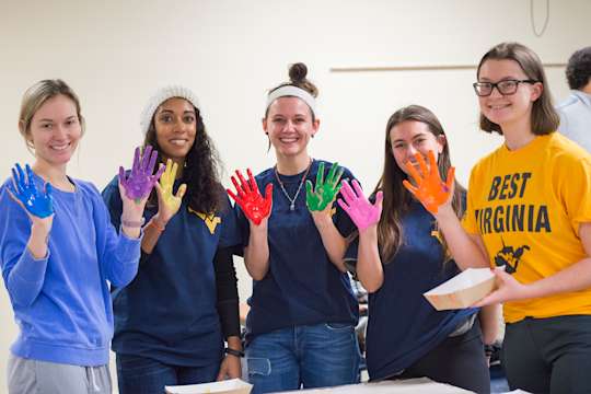 A group of students shows different colors of paint on the palms of their hands. They were part of a project to paint a mural at a local school.