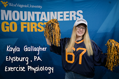 Kayla Gallagher, an Exercise Physiology major from Elysburg, PA, raises gold and blue pom poms in the air.