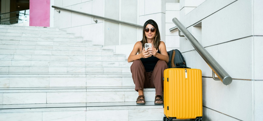 Woman sitting with her suitcase, looking at her phone