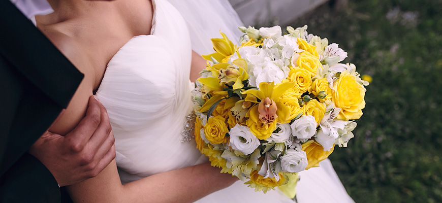 A photo of a couple about to be married. A beautiful yellow bouquet is held by the bride. 