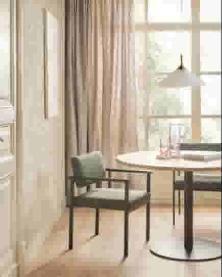Kamer met lichte vitrages voor de ramen en een ronde tafel met groene stoelen
