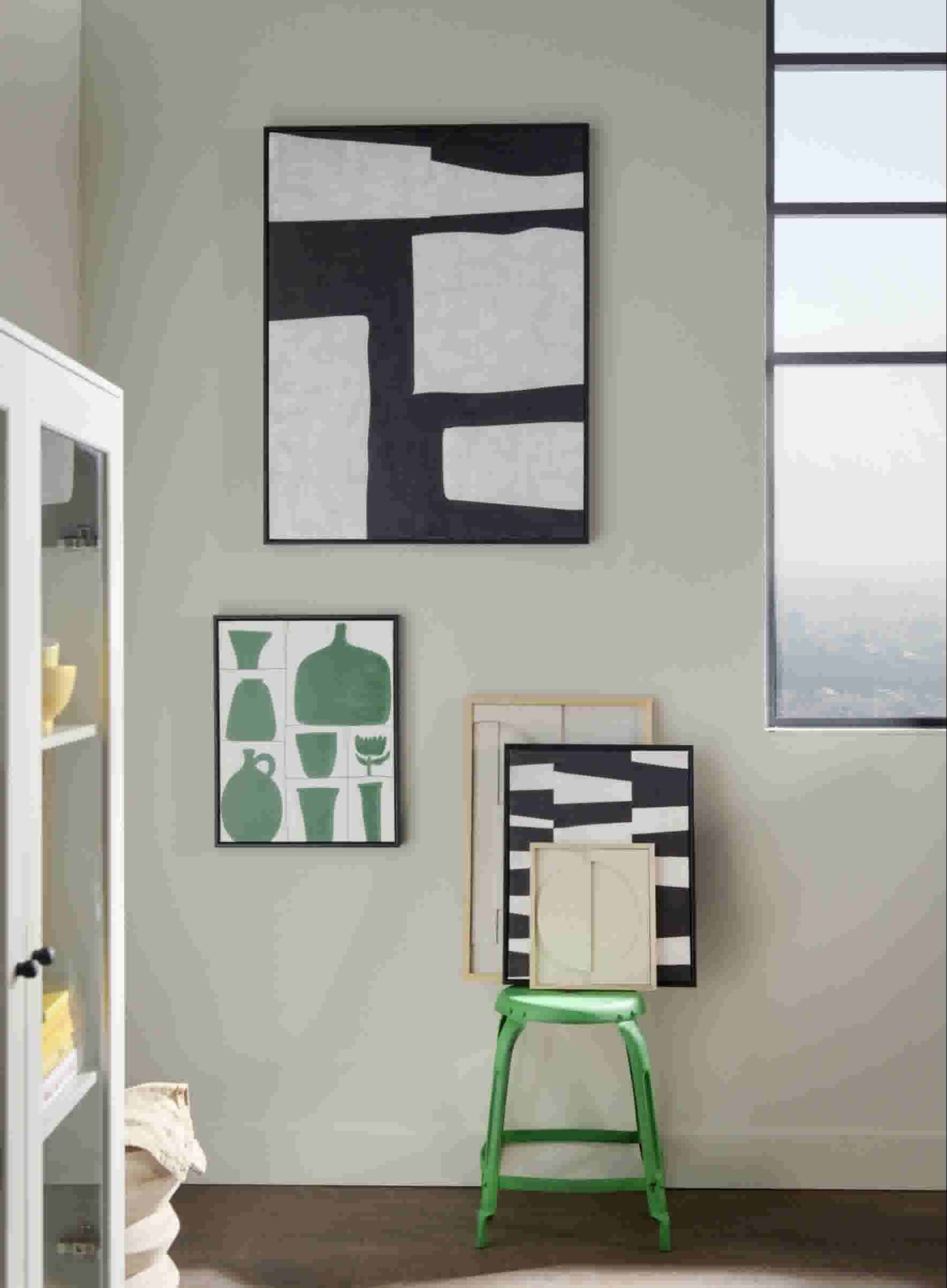 Schilderijen hangend aan een beige muur boven een groene kruk