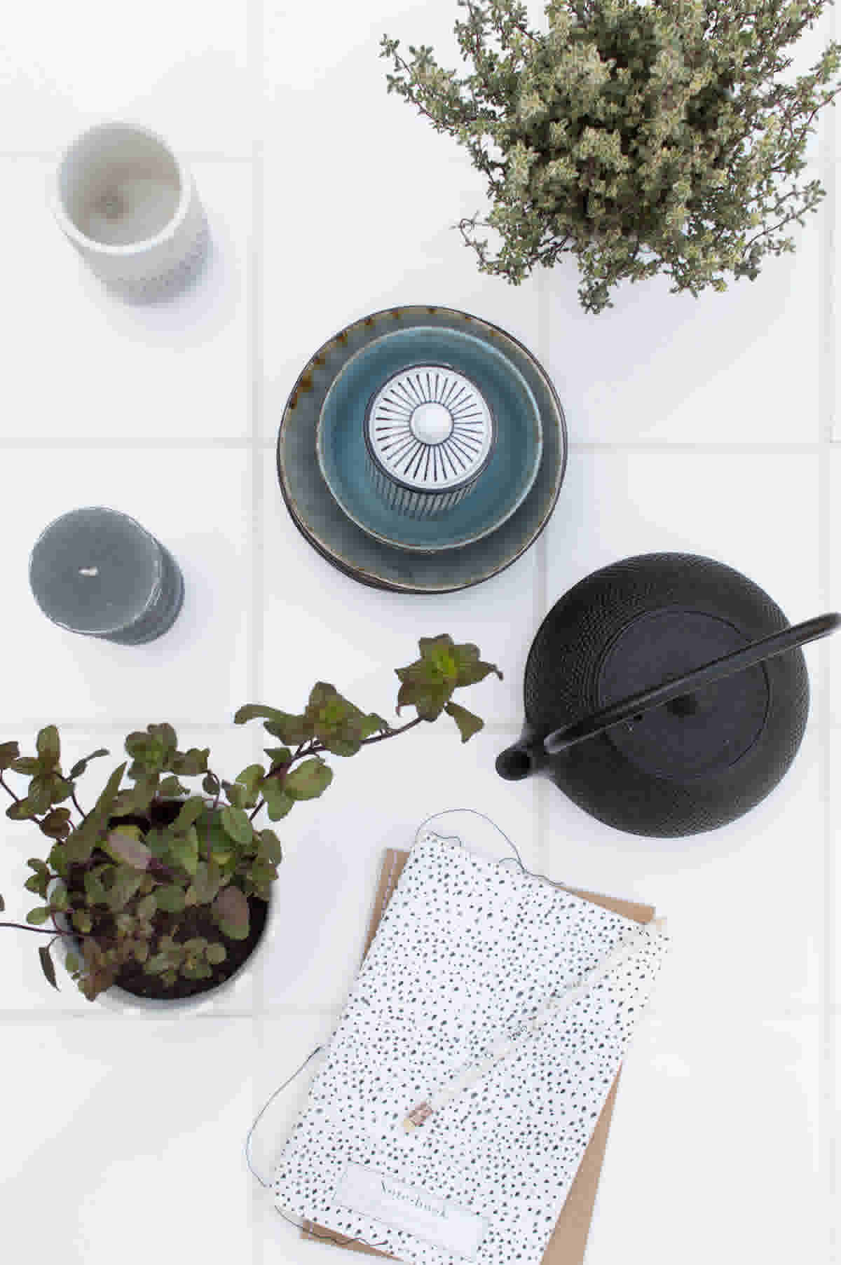 Tuintafel van witte tegels met theepot, notitieboek, kaars en plant