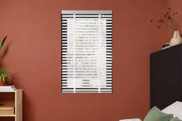 Wit raam met zwart-witte horizontale jaloezieën tegen een terracotta oranje muur in een moderne slaapkamer.