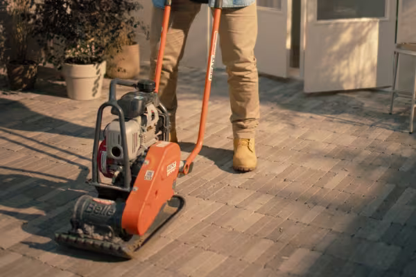 Gehuurde trilplaat in gebruik voor het verdichten van bestrating op een terras