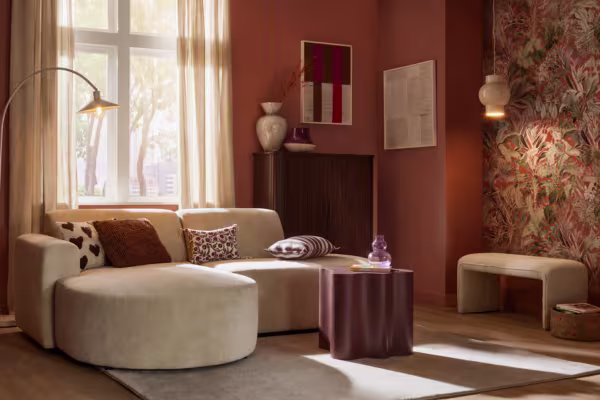 Warme woonkamer met beige ronde bank, bruine salontafel, terracotta muren, bloementapijt en natuurlijk licht via gordijnen.