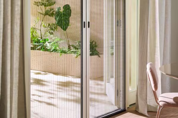 Hordeuren met verticale strepen die uitkijken op een zonnig terras met groene planten en een lichte stoel in de kamer.