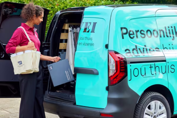 Karwei adviseur haalt map uit turquoise Karwei bus met tekst 'Persoonlijk advies bij jou thuis', met tas over schouder.