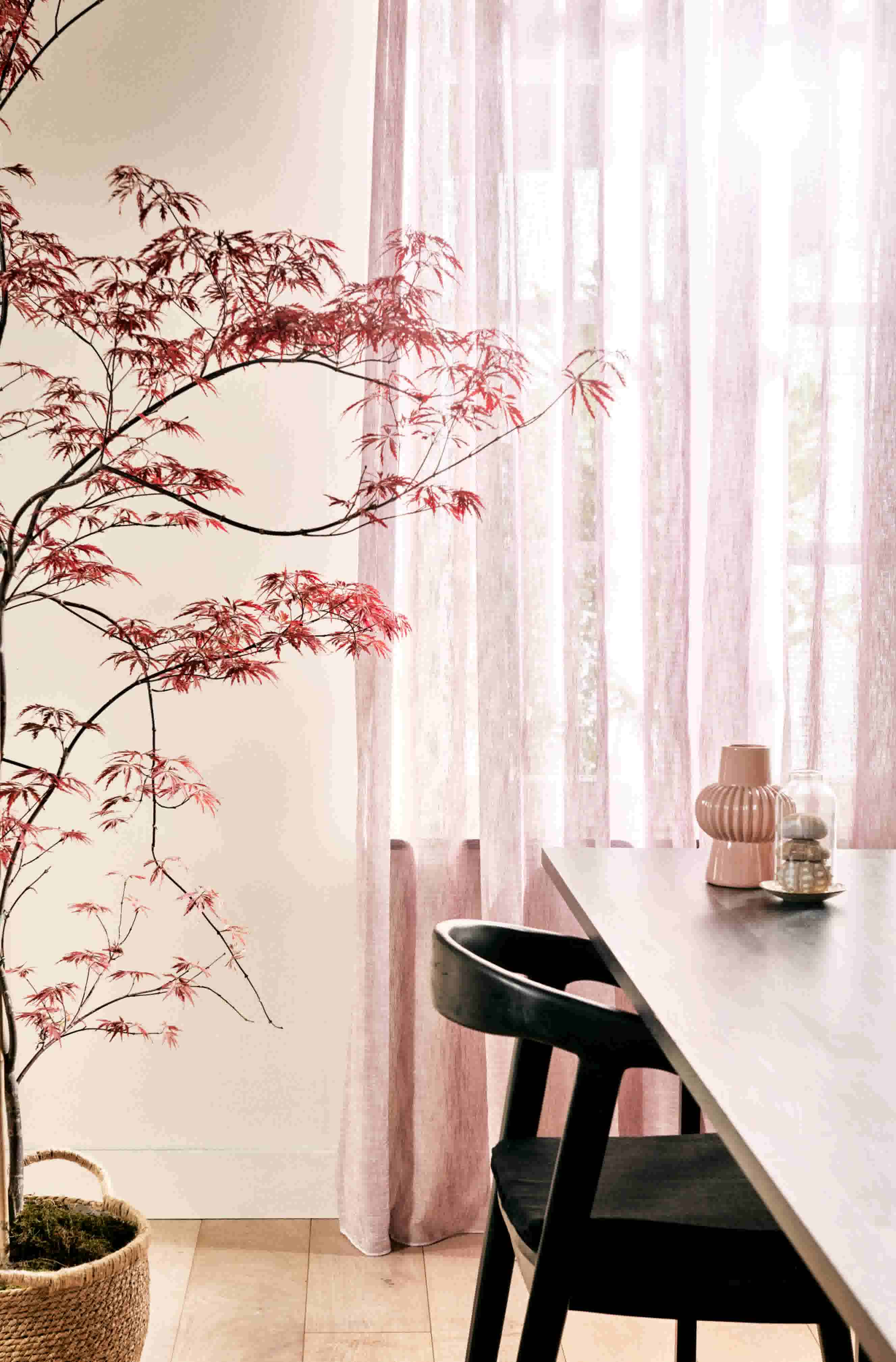 Lichtroze doorschijnende gordijnen in een kamer met een tafel en bloesemboom