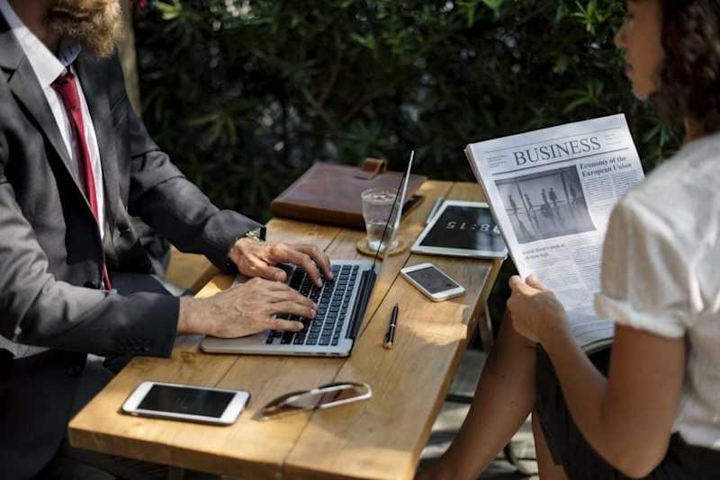 Photo of someone using a laptop and someone reading a newspaper