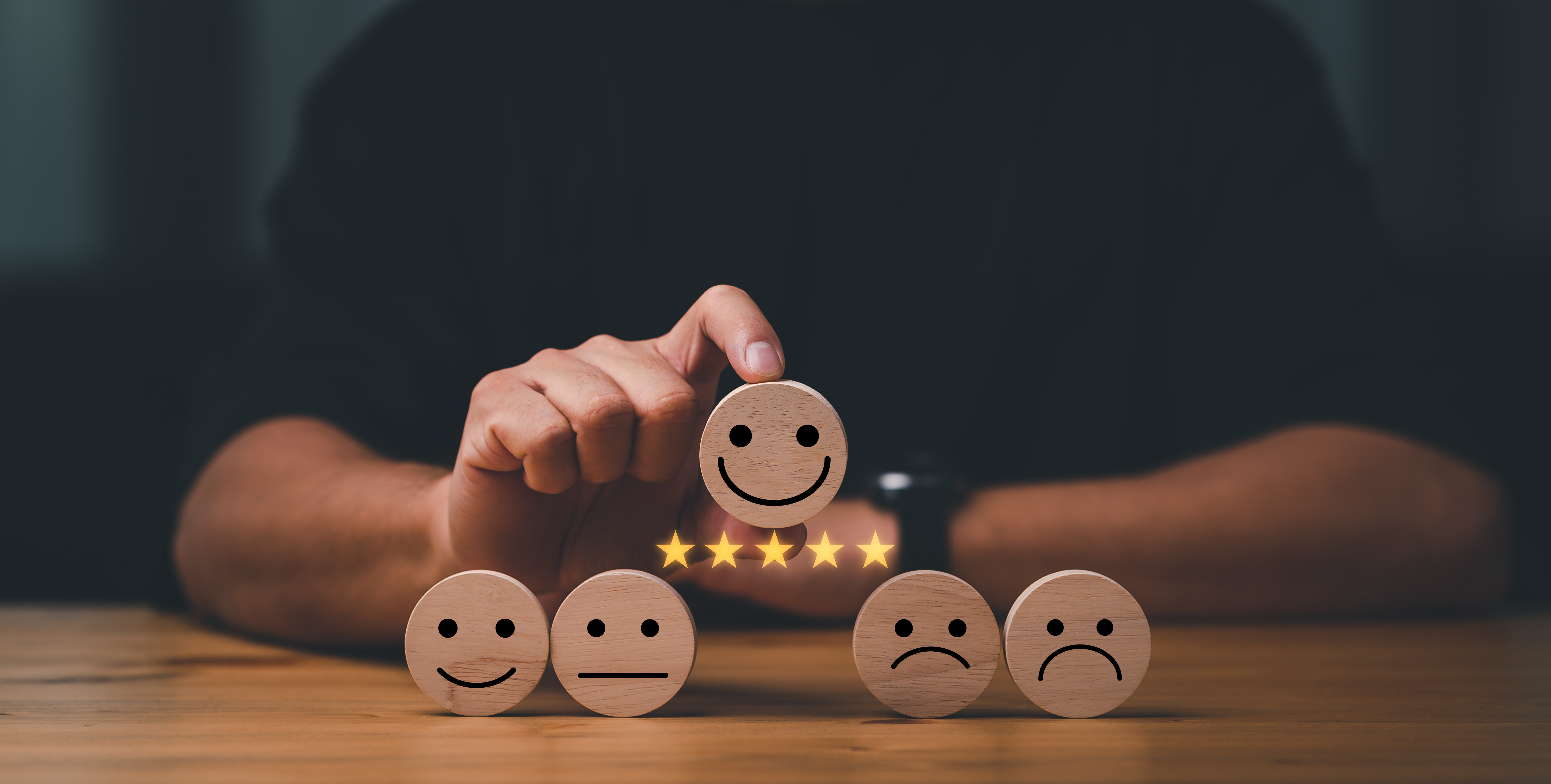 An image showcasing five smileys and five stars. A person is lifting up a smiling smiley in the middle. The smiling smiley represents a happy customer and the five stars represent the NPS score.