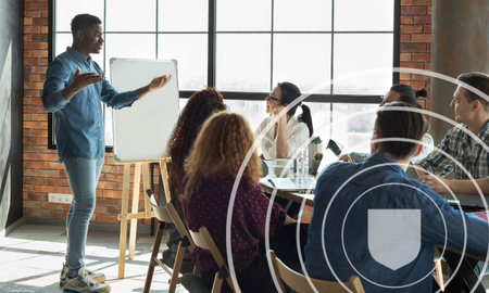 man stood next to a whiteboard leading a group of people sat around a table