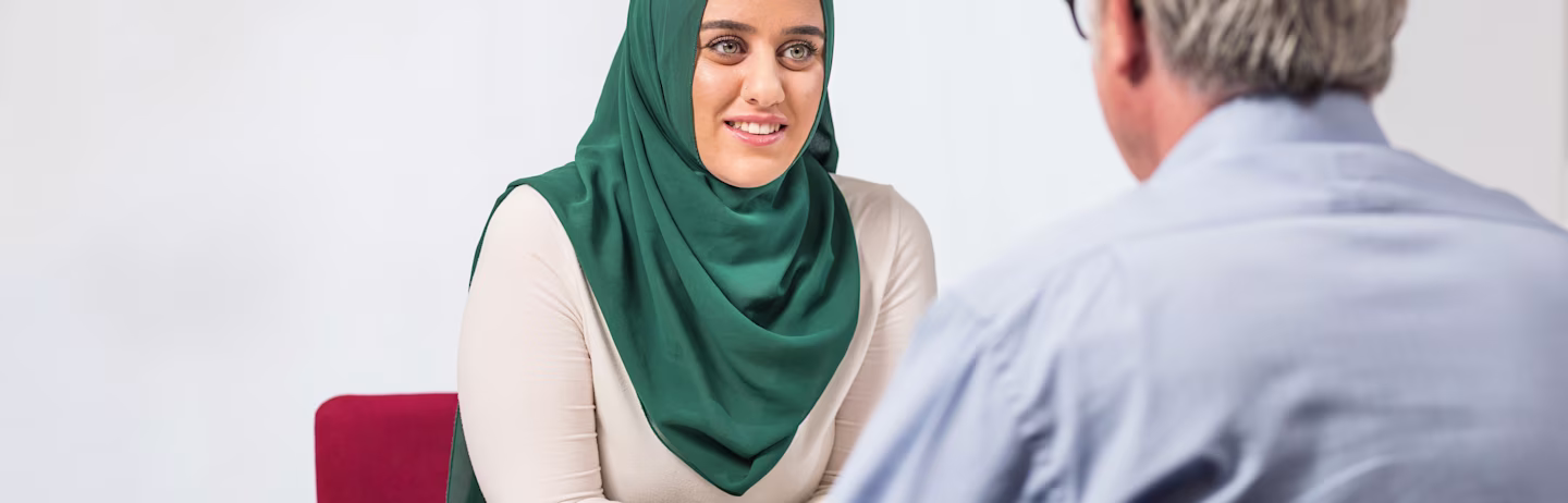 A female IELTS test taker in a green headscarf taking the IELTS Speaking test