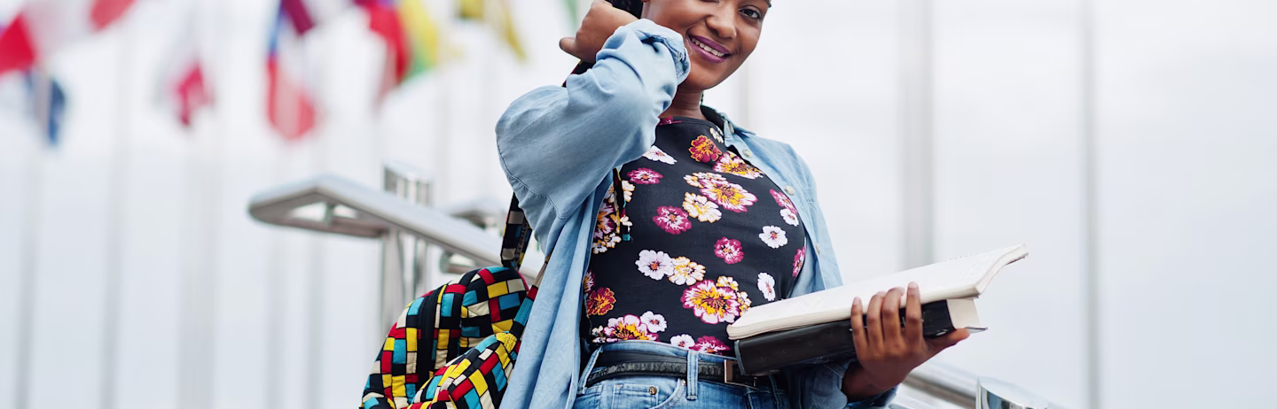 A female student wearing a flowers printed t-shirt and denim overcoat with a backpack on walks down some stairs