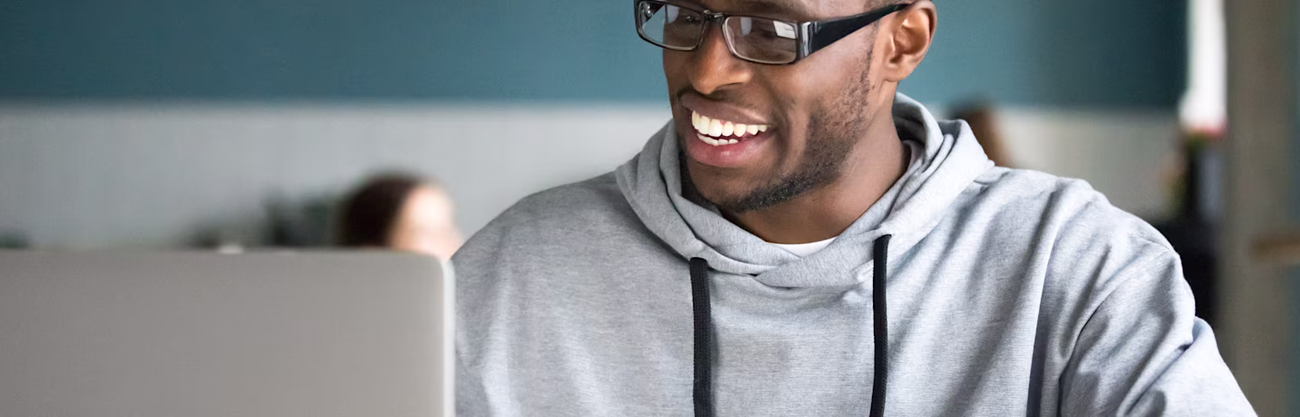 A male IELTS test taker wearing a grey hoodie and glasses prepares for IELTS on his computer