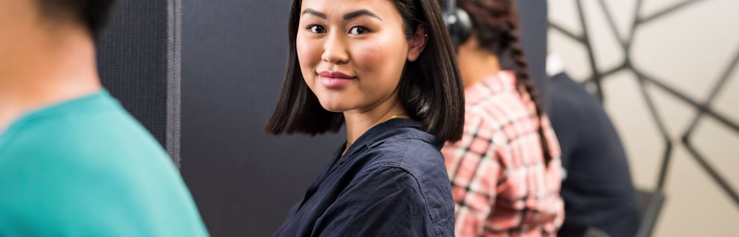 Female IELTS test taker wearing a dark blue shirt with headphones attending a computer-delivered IELTS test