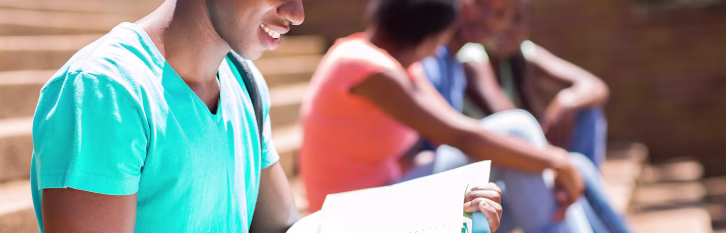 Photograph of a male student sitting on the steps and reading a book.