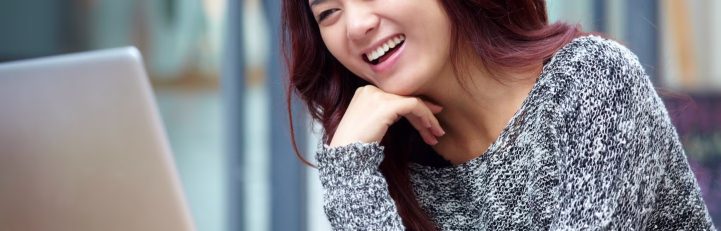 A female test taker wearing a grey top looks at her laptop and prepares for IELTS.