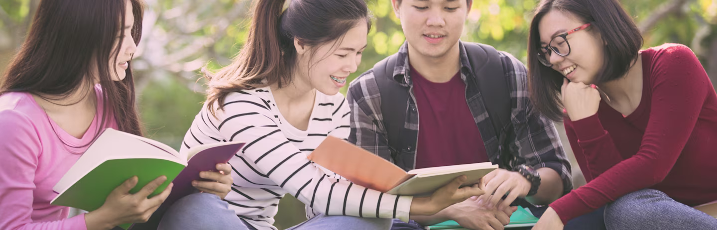 Three female test takers and a male test taker in western outfits siting on grass with IELTS official preparation materials