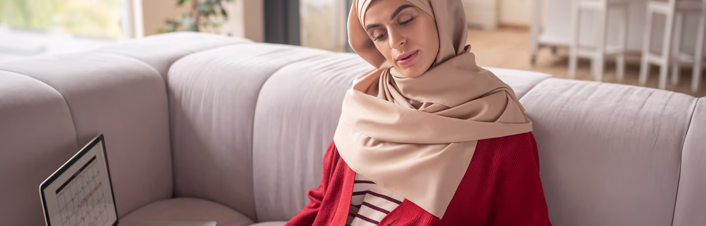 A female test taker reads IELTS preparation materials with a laptop on the couch