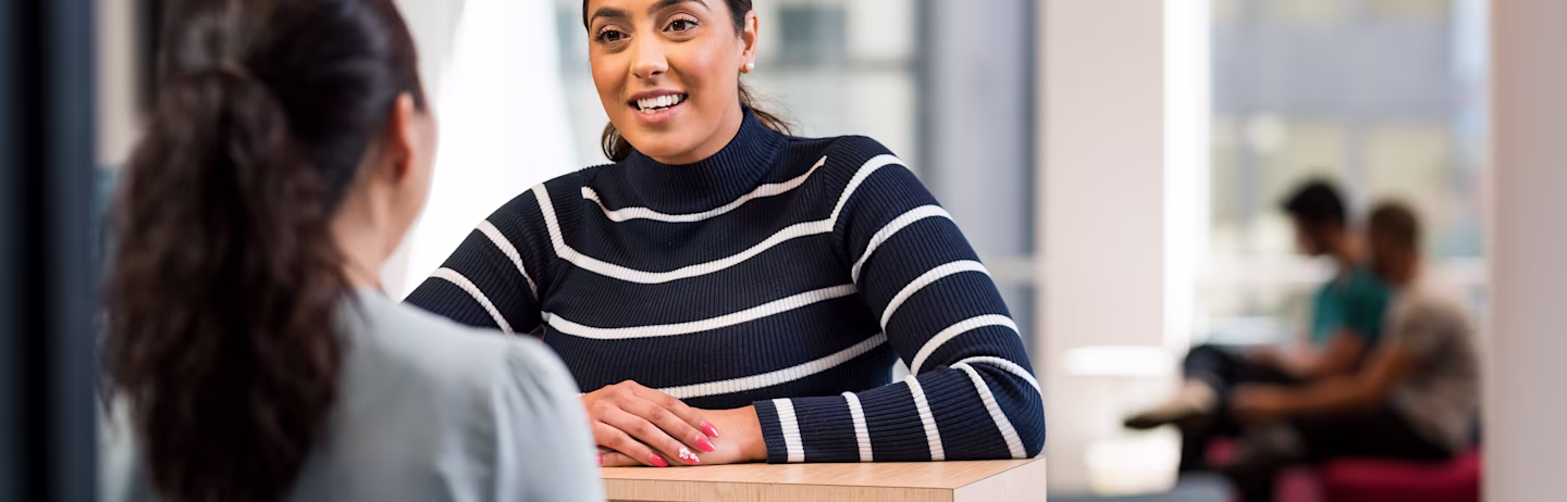 Female IELTS test taker makes an enquiry about the test in an IELTS test centre with an IELTS staff