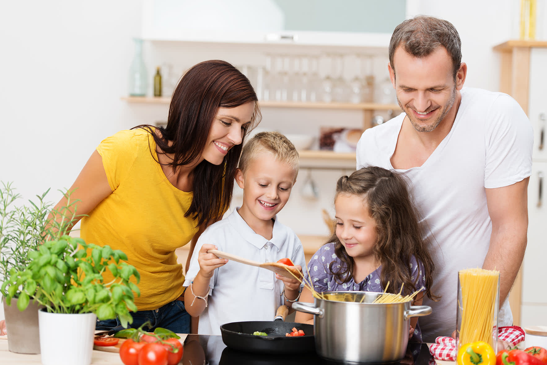 Eltern mit zwei Kindern stehen um den Herd und kochen zusammen