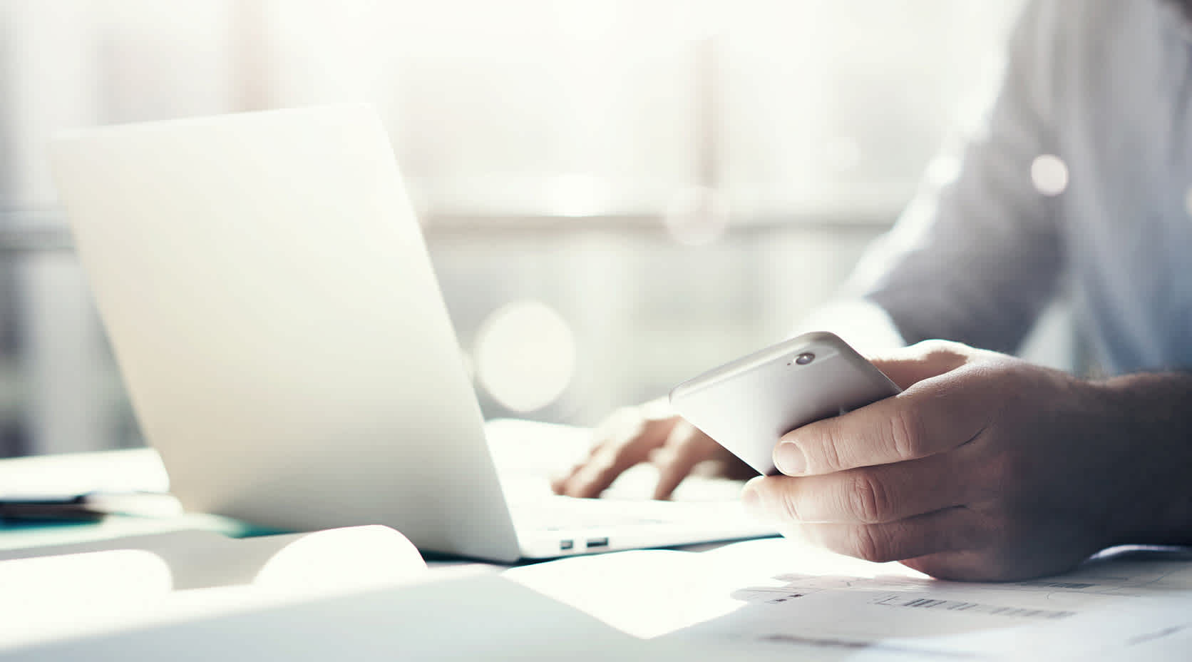 Mann mit Smartphone arbeitet an Notebook