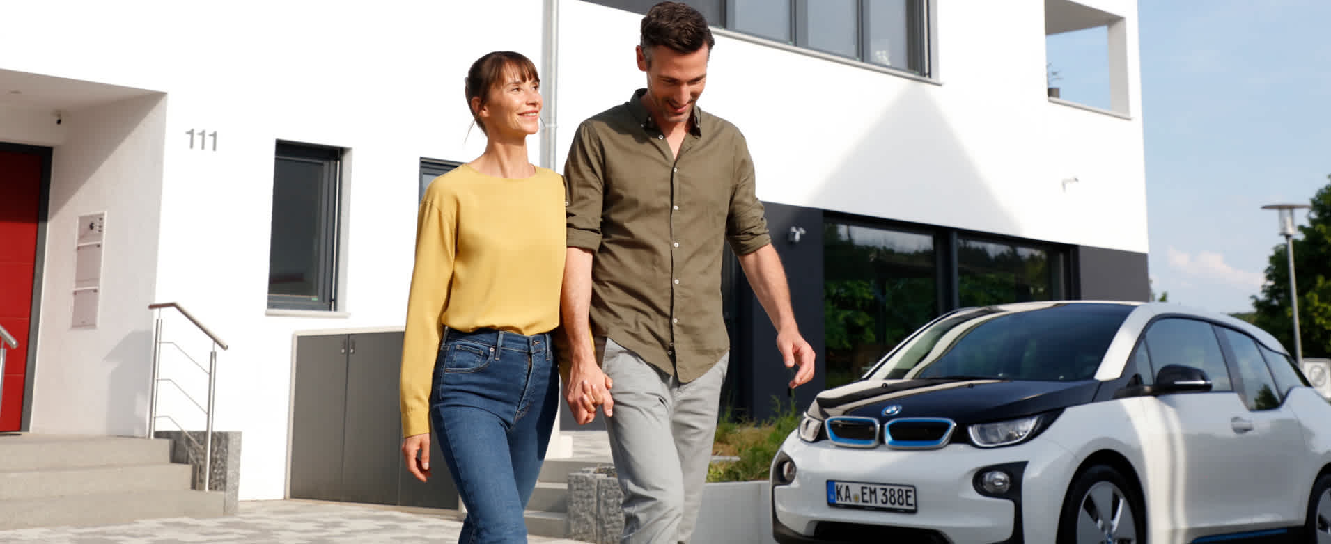 Paar beim entspannten Spaziergang vor Haus mit E-Auto