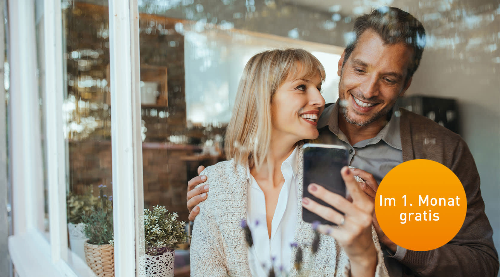 Mann und Frau stehen am Fenster und schauen aufs Handy