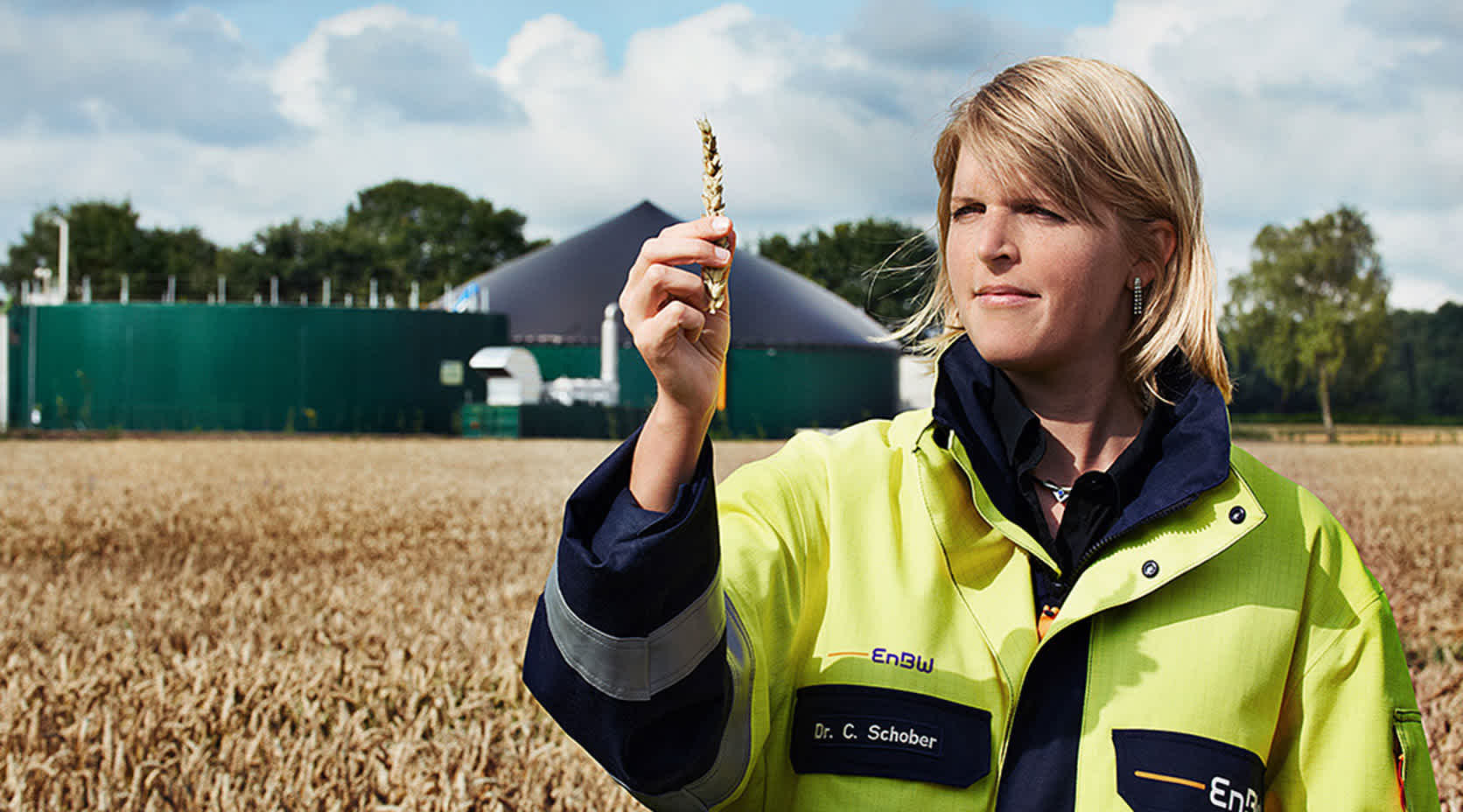 EnBW-Mitarbeiterin steht vor Biogasanlage, hat Ähre in der Hand.