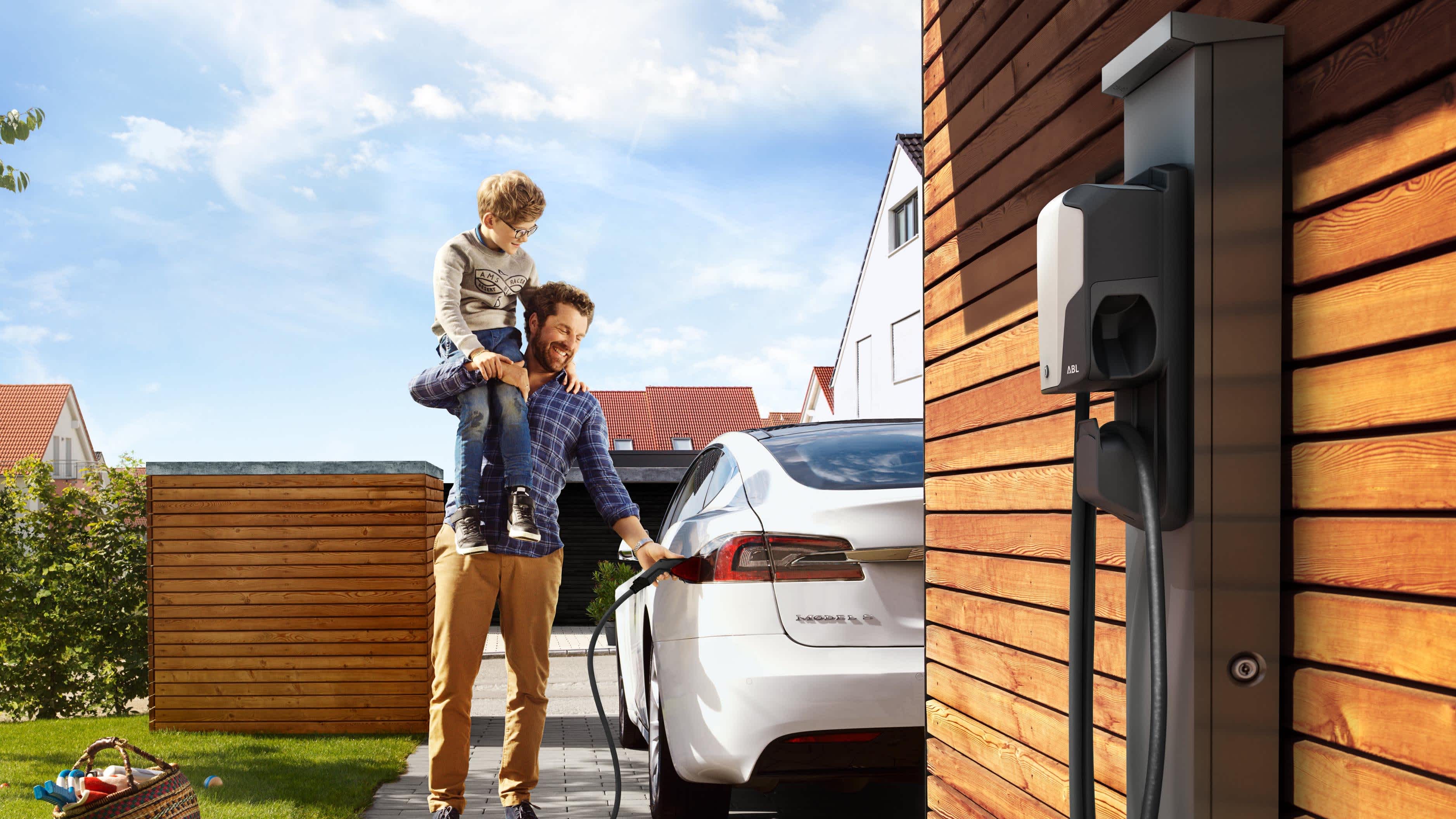 Mann mit Kind auf Schulter lädt E-Auto auf, EnBW mobility+ Wallbox im Vordergrund