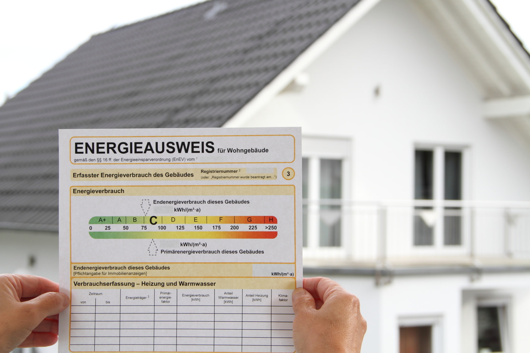 Person hält einen Energieausweis vor dem Haus