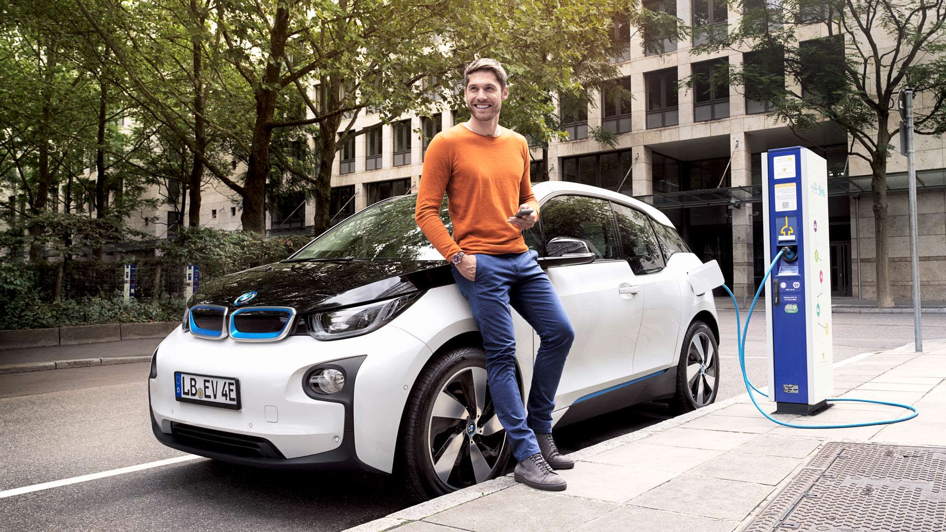 Mann lehnt an Elektroauto, welches an EnBW-Ladestation aufgeladen wird