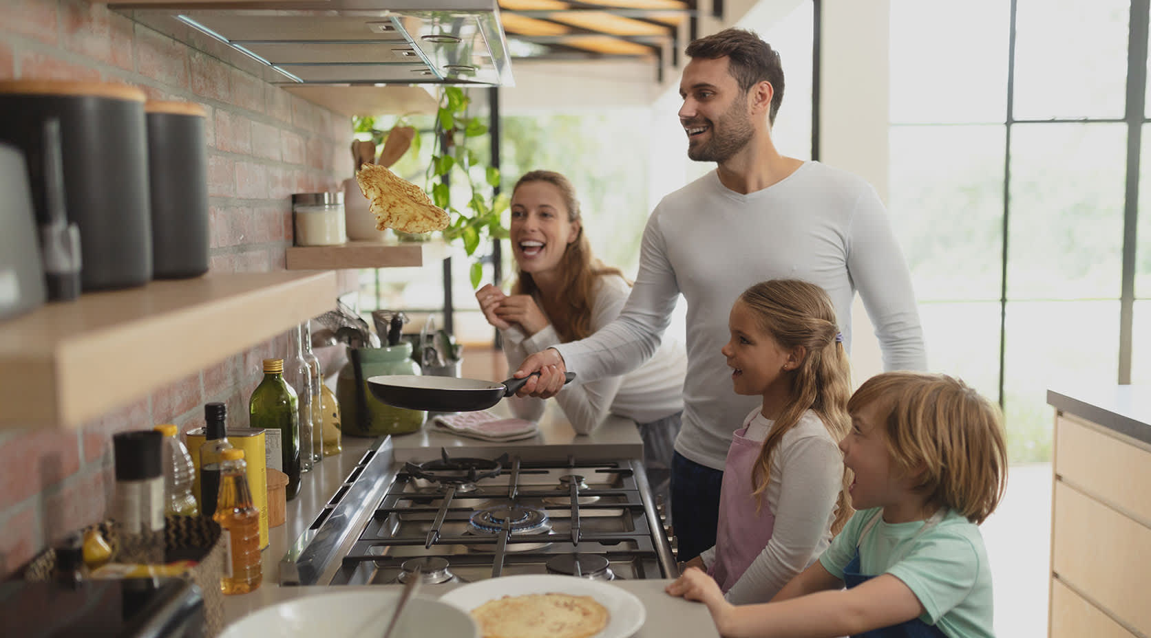 Familie backt Pfannkuchen an Gasherd. Vater wendet Pfannkuchen wie Profi.