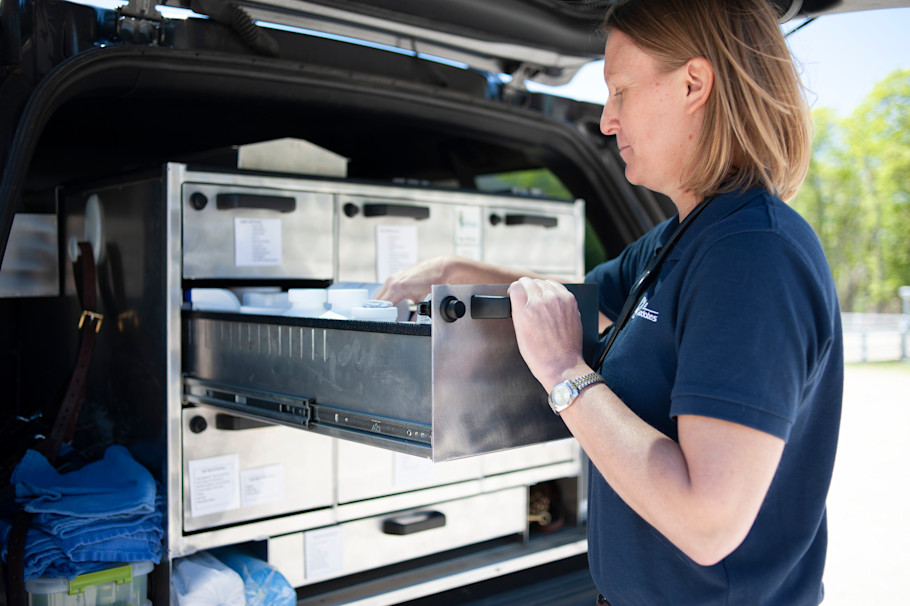 An equine veterinarian taking horse medicine bottles from her truck.