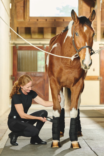 A woman putting ice boots on a horse's legs.