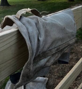 A fly boot resting on a fence rail, with a grey strip of binding fabric on the boot poking up away from the mesh.