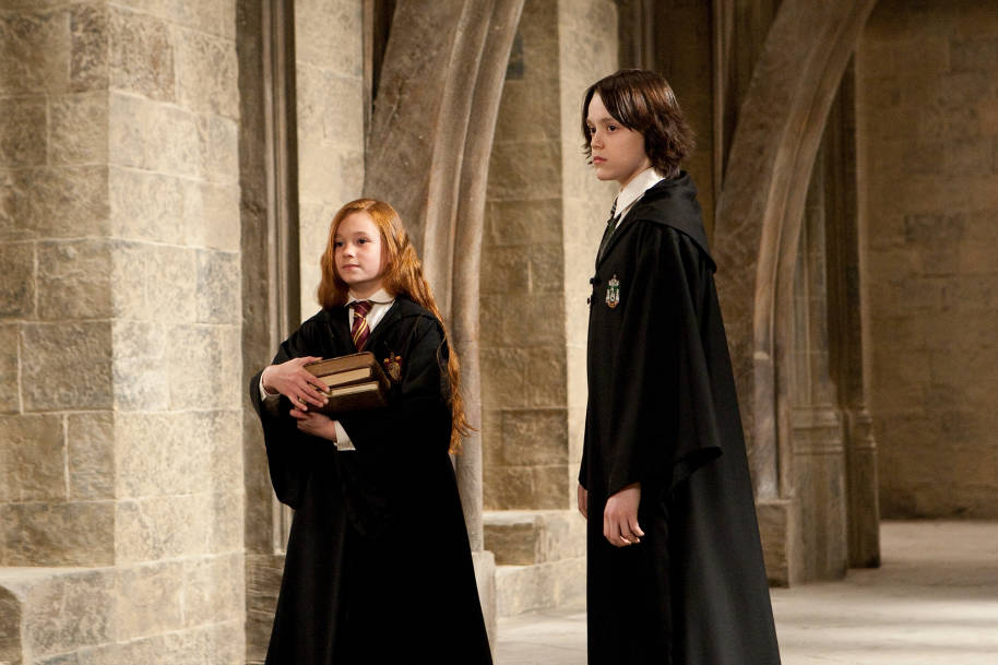 A young Lily and Snape in the corridors of Hogwarts. Lily is carrying a pile of books.