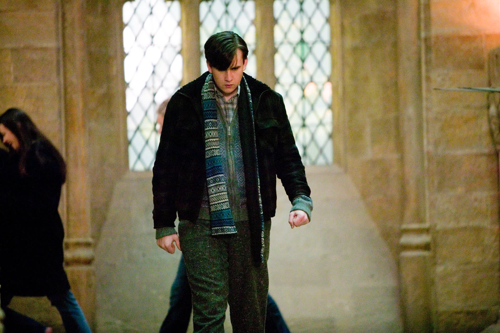 Neville Longbottom walking through Hogwarts wrapped up in a blue scarf.