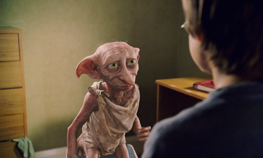 Dobby is in Harry's bedroom at 4 Privet Drive. He is smiling at Harry.