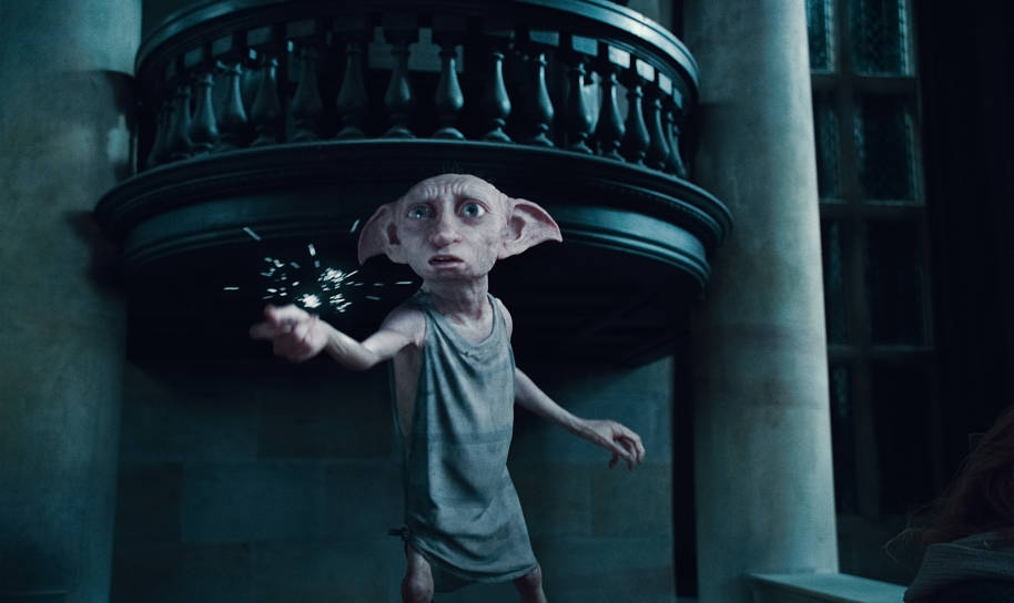 Dobby is standing in Malfoy Manor with his arm outstretched. He is using magic, snapping his fingers which has created sparks.