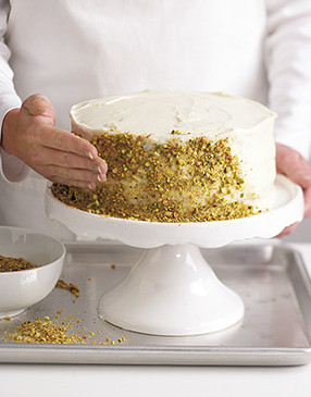 Press pistachios onto the cake with your palm. To catch any stray nuts, place the cake stand on a baking sheet.