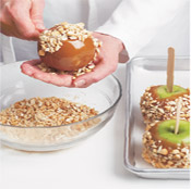 After coating each apple with caramel, use your hand to press the topping into the warm caramel.