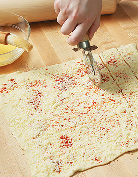 Season the puff pastry sheet with salt, paprika, and Parmesan, then use a pizza wheel to cut it into squares.