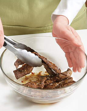 After grilling, toss the beef in some sauce to coat — it'll help the sesame seeds and scallions stick.