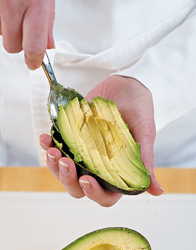 Pit the avocado half and cut flesh into slices with a knife. Scoop out the slices easily with a spoon.