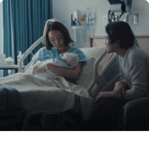 躺於醫院病床的女性抱著新生兒,父親坐在床邊。