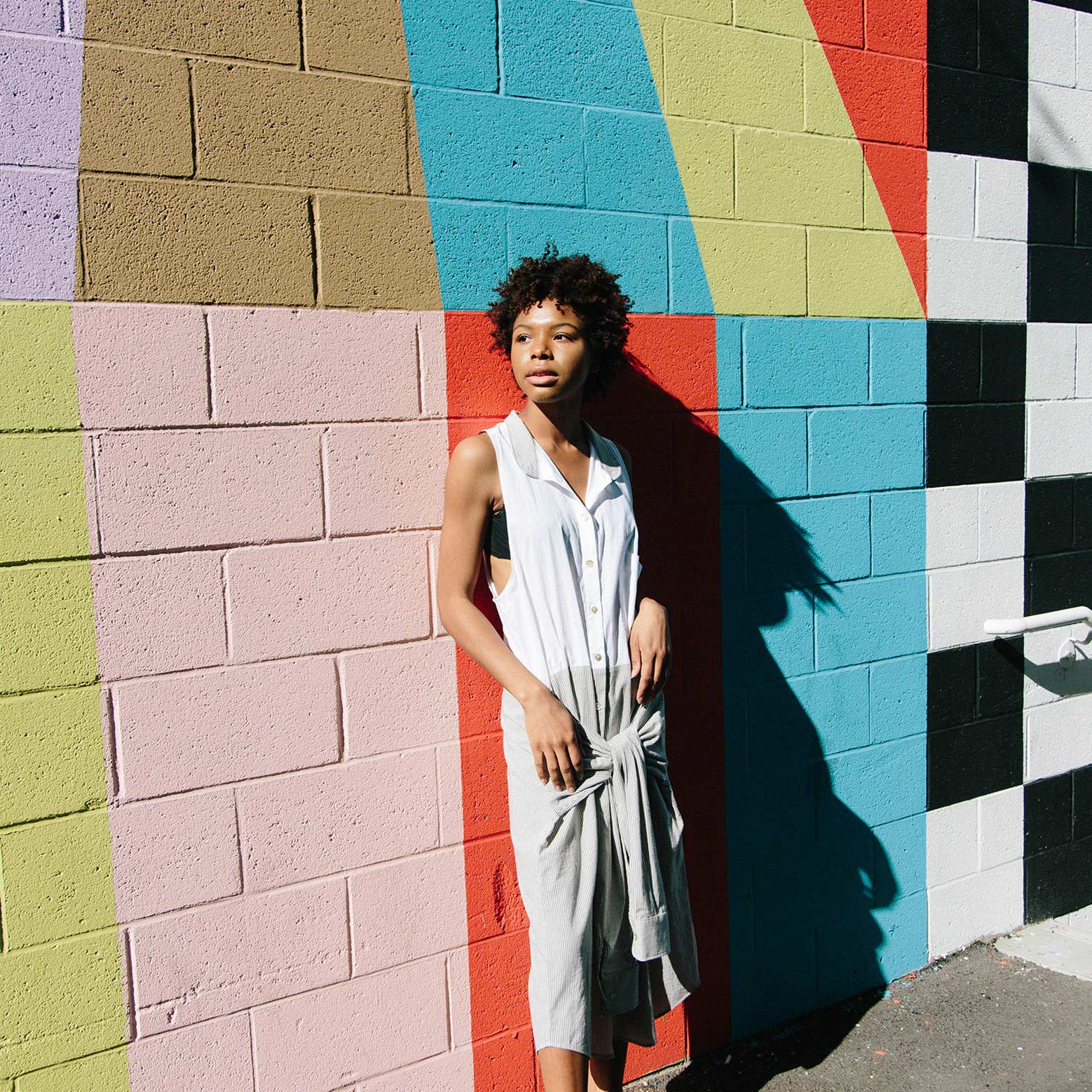 woman wearing white dress with back against painted color graffiti wall